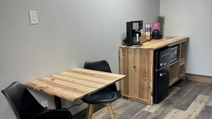 A room with a wooden table and chairs, a kitchenette with a coffee machine, and an air conditioning unit on the wall. - Soothing 1-bedroom hotel room with AC in Raystown Lake Region (Huntingdon)