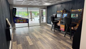 Een kamer met een houten vloer, een groot raam en twee speelautomaten.