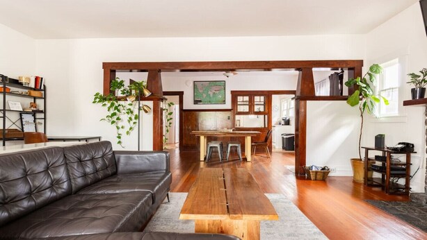 A spacious living area with a leather sofa, wooden coffee table, and a dining table with chairs. There are plants, bookshelves, and a kitchen in the background. - Craftsman 2 blocks from Russian River Brewery! (Santa Rosa)