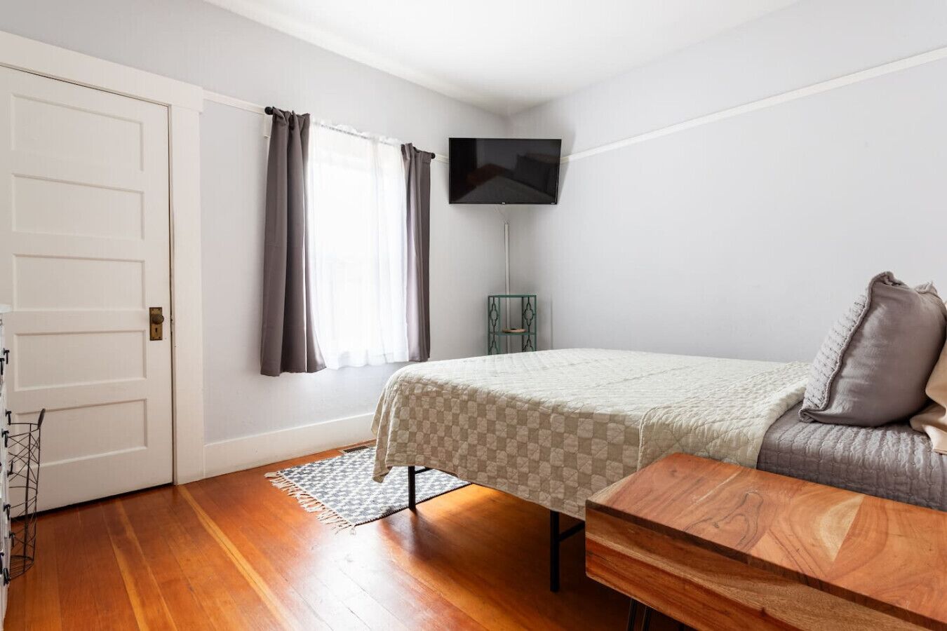 Een slaapkamer met een bed, een aan de muur bevestigde televisie en een houten bankje.