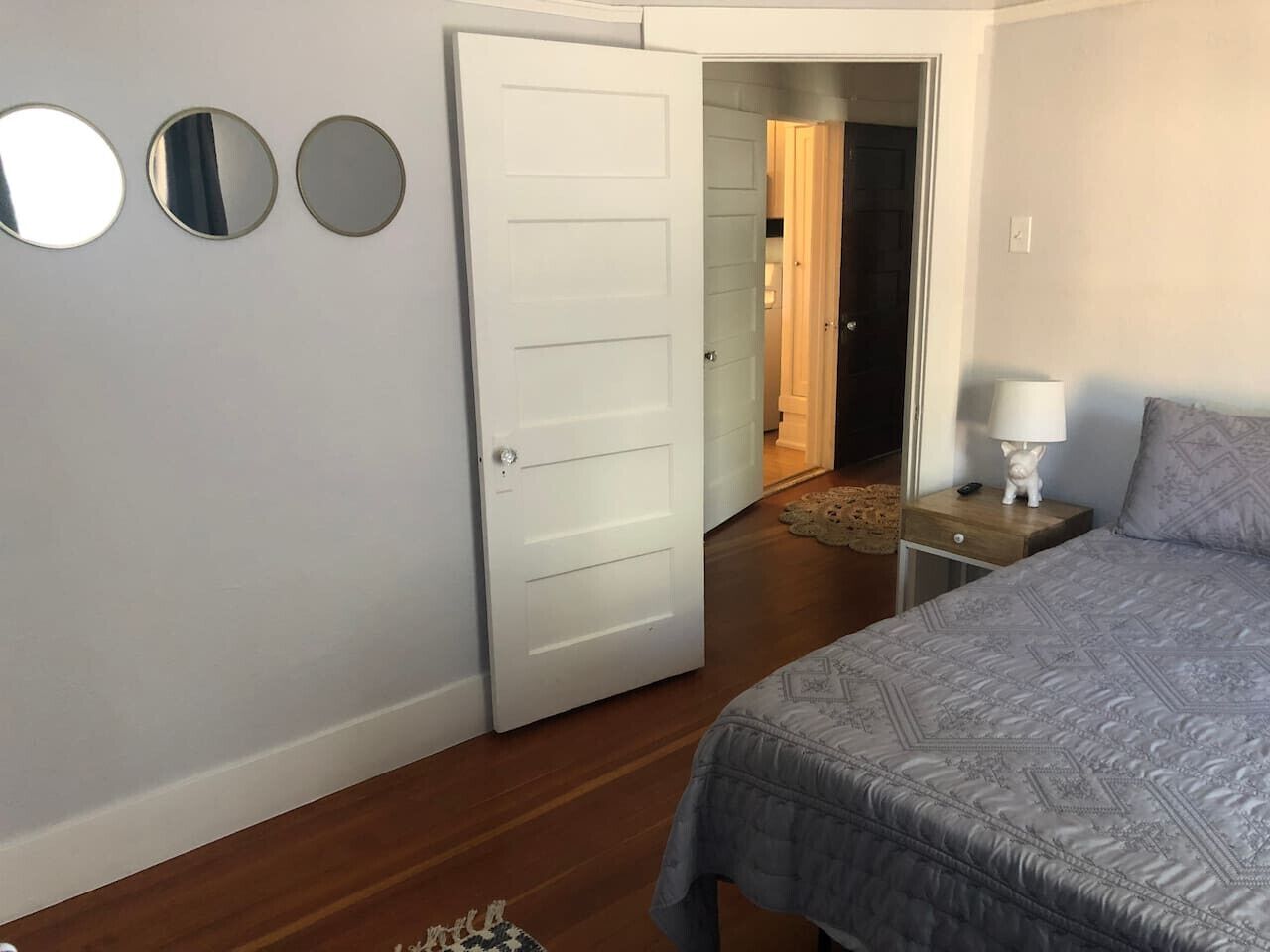 Una camera da letto con un letto, un comodino, una lampada e una porta che dà su un'altra stanza.