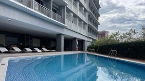 Piscina com espreguiçadeiras, boia salva-vidas e um arbusto.