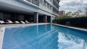 Une piscine avec des chaises longues, une bouée de sauvetage et une haie.