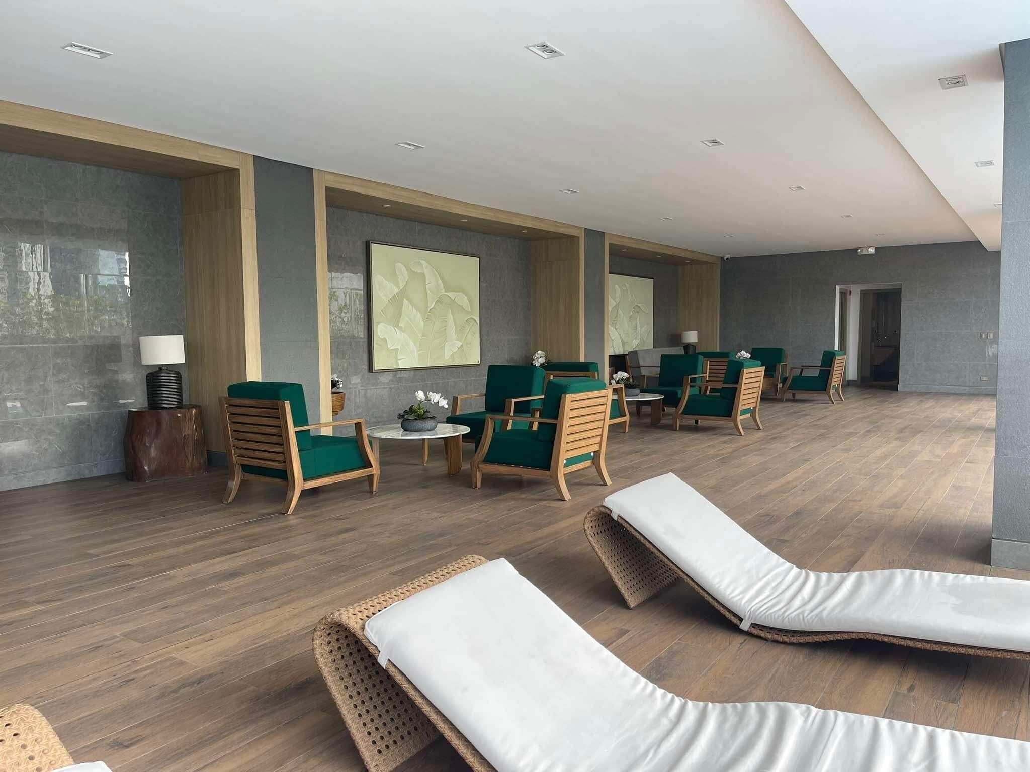 Un espace de détente moderne avec des fauteuils en osier, des chaises à revêtement vert et une table centrale agrémentée d’une lampe et de fleurs.