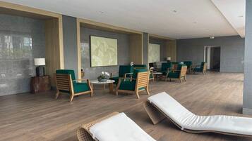 Un espace de détente moderne avec des fauteuils en osier, des chaises à revêtement vert et une table centrale agrémentée d’une lampe et de fleurs.