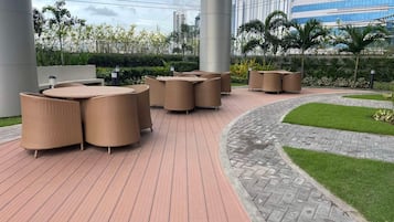 Un espace extérieur aménagé avec des meubles en osier, une terrasse dallée et un jardin paysager agrémenté de pelouse et de plantes.
