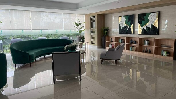 Uma sala de estar espaçosa e moderna, com um sofá verde curvo, uma poltrona cinzenta e uma estante de madeira.