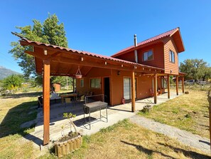 A wooden house with a red roof, a covered patio with outdoor furniture, and a stone pathway.
