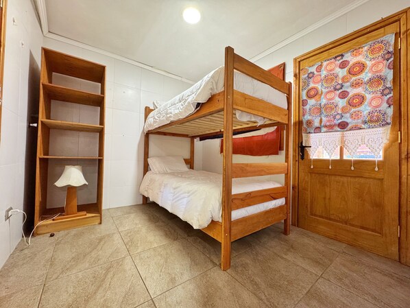 A bunk bed room with a wooden door, a shelf unit, and a window with a patterned curtain.
