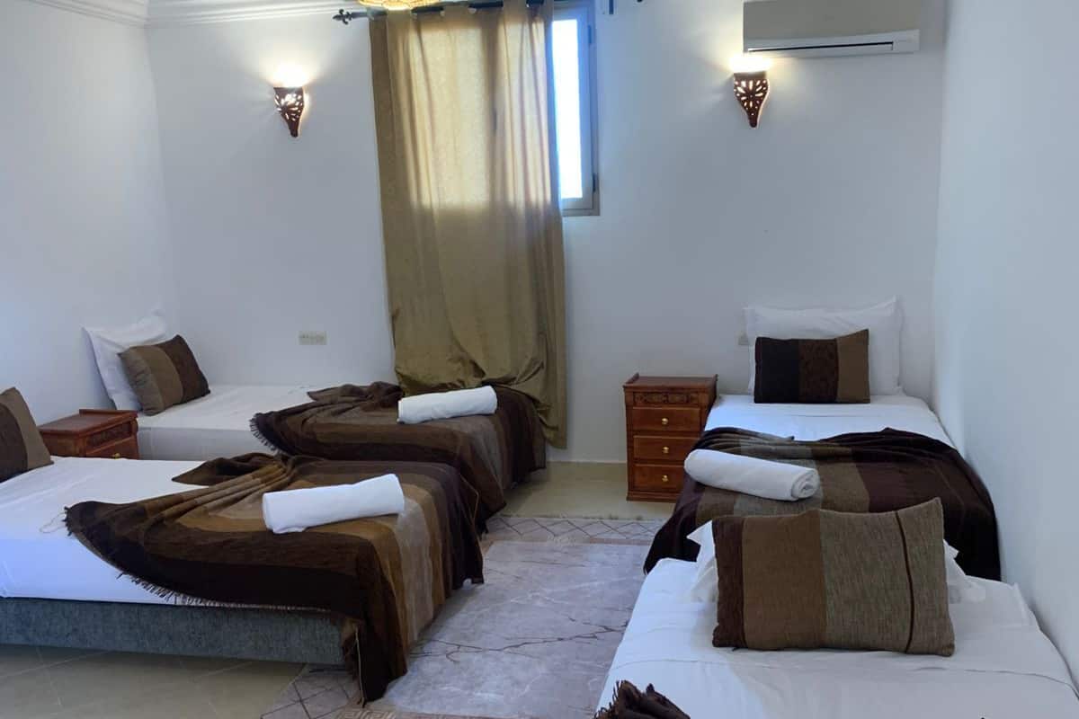 A hotel room with three beds, a chandelier, an air conditioner, and a window with curtains.