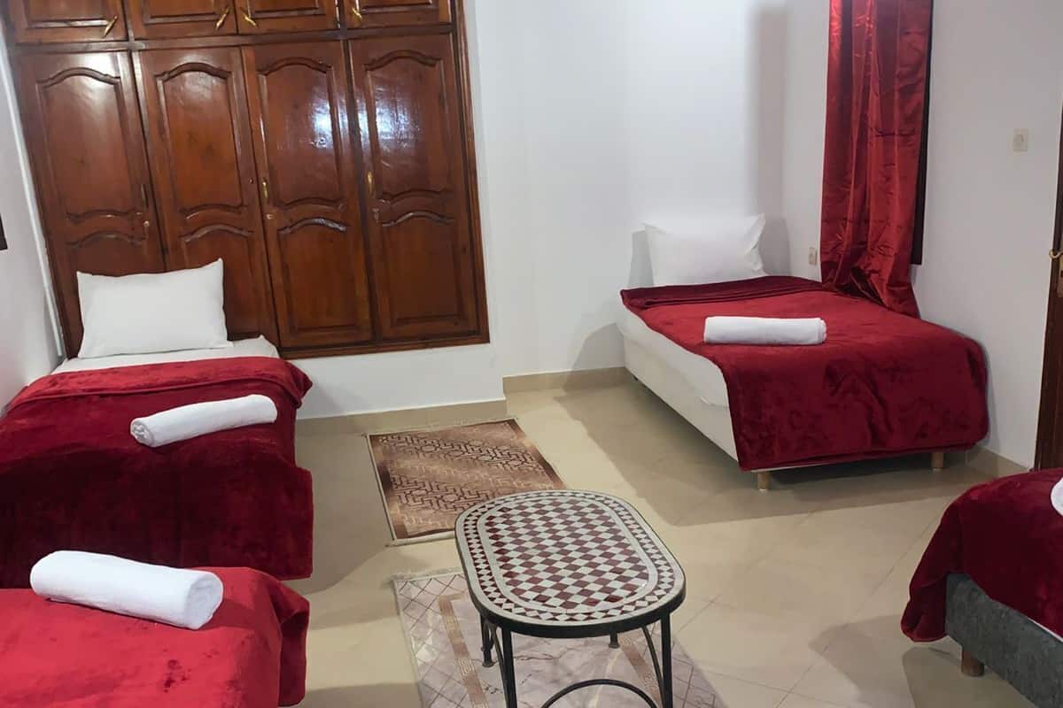 A room with two beds, a small table, a wooden wardrobe, and a patterned rug.