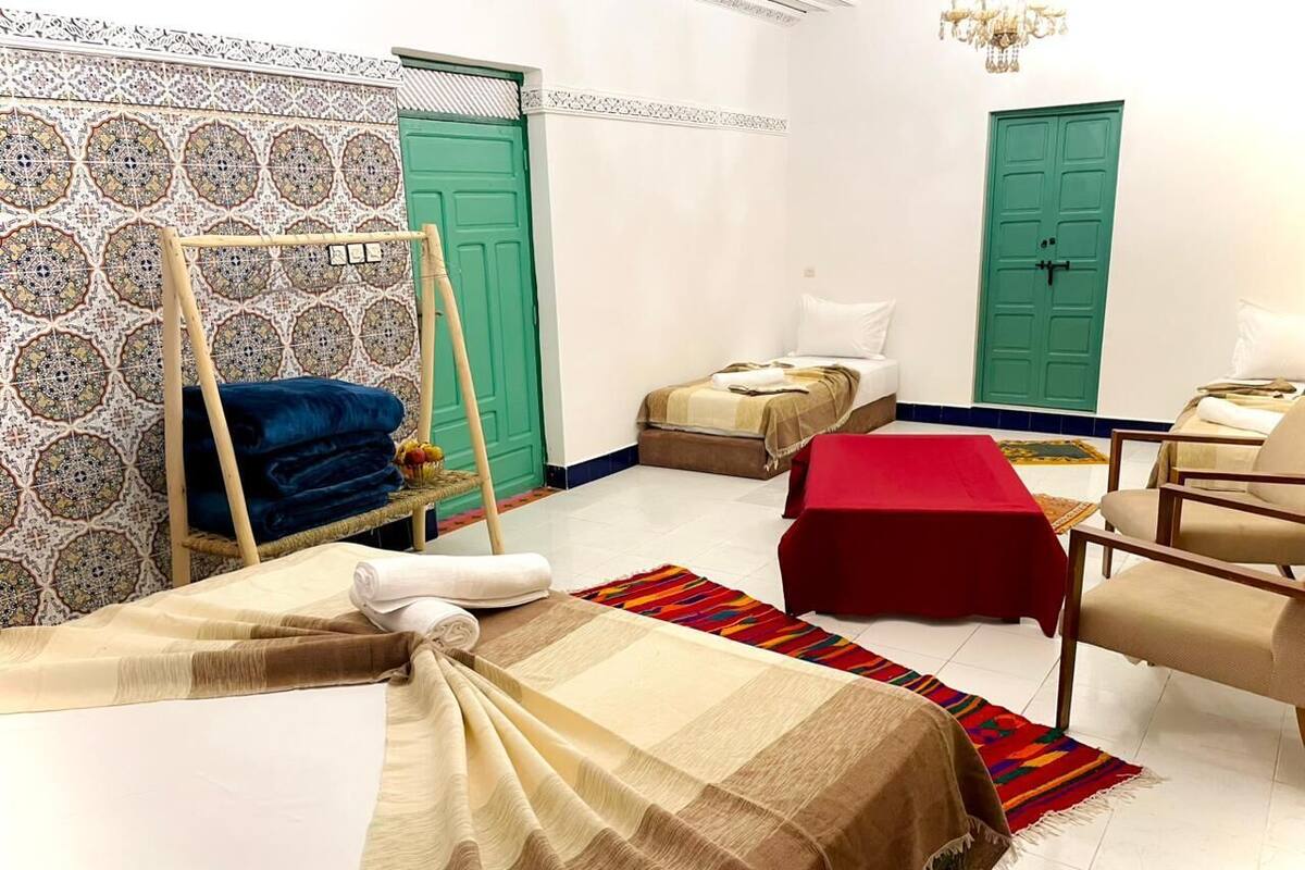 A hotel room with a bed, a chair, a table, and two doors.