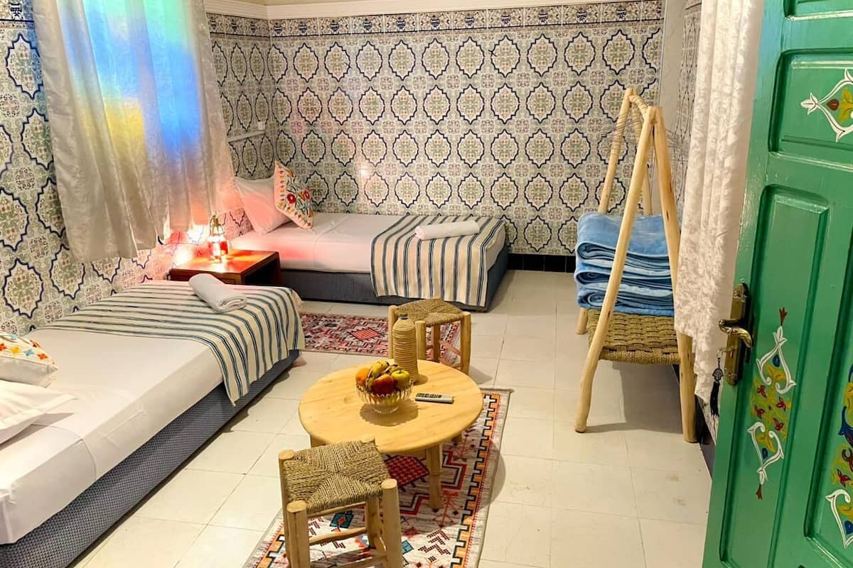 A cozy room with a bed, a sofa, a small table with fruit, a chair, and a green door.