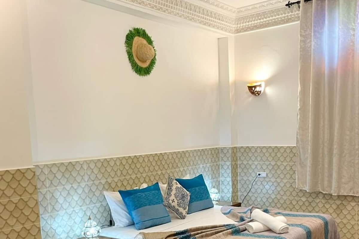 A bedroom with a bed, bedside tables, a small round table with fruit, a colorful rug, and a patterned wall.