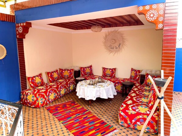 A room with a central round table, multiple sofas with colorful upholstery, and a patterned floor. - riad la joie (Marrakech)