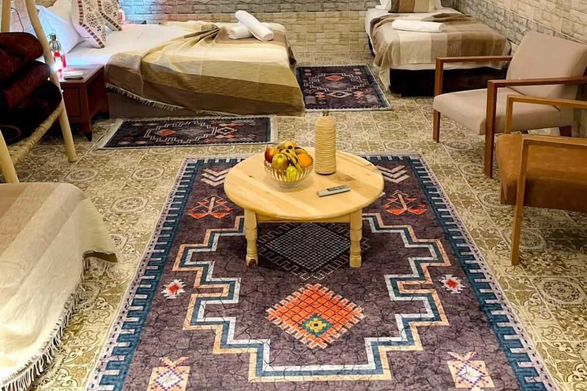 A cozy room with two beds, a small table with fruit, a chair, and a patterned rug.