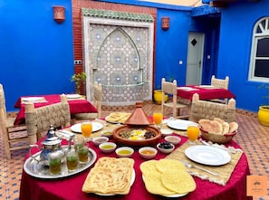 A traditional Moroccan dining setup with a table set for two, featuring a tagine, flatbreads, and various dishes. - riad la joie (Marrakech)
