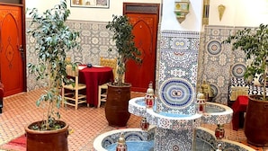 Un interior marroquí tradicional con una fuente, plantas en macetas y baldosas con diseños.