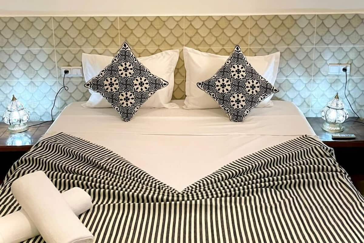 A hotel room with a bed, striped bedding, patterned pillows, a decorative wall, and a wall-mounted light fixture.