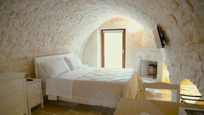 Ein Schlafzimmer mit Steindecke, einem Bett mit weißer Bettwäsche, einem Nachttisch, einem Stuhl und einem Tisch mit Lampe.