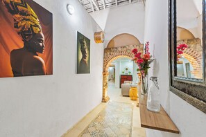 Ein Korridor mit Fliesenboden, einem Spiegel, einer Vase mit Blumen und einem Gemälde an der Wand.