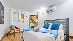 Un dormitorio con cama, una silla, un ventanal y un equipo de aire acondicionado.
