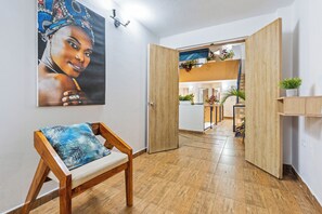 Ein Zimmer mit einer hölzernen Bank, einem Bild an der Wand und einer offenen Tür, die in einen weiteren Raum mit Pflanzen führt.
