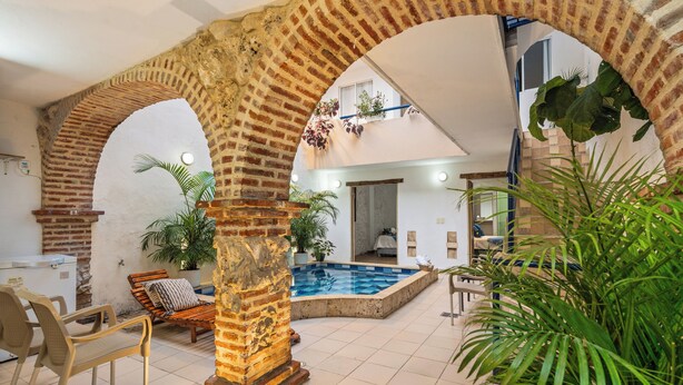 Zona de piscina interior con arcos de ladrillo, asientos y plantas en macetas.