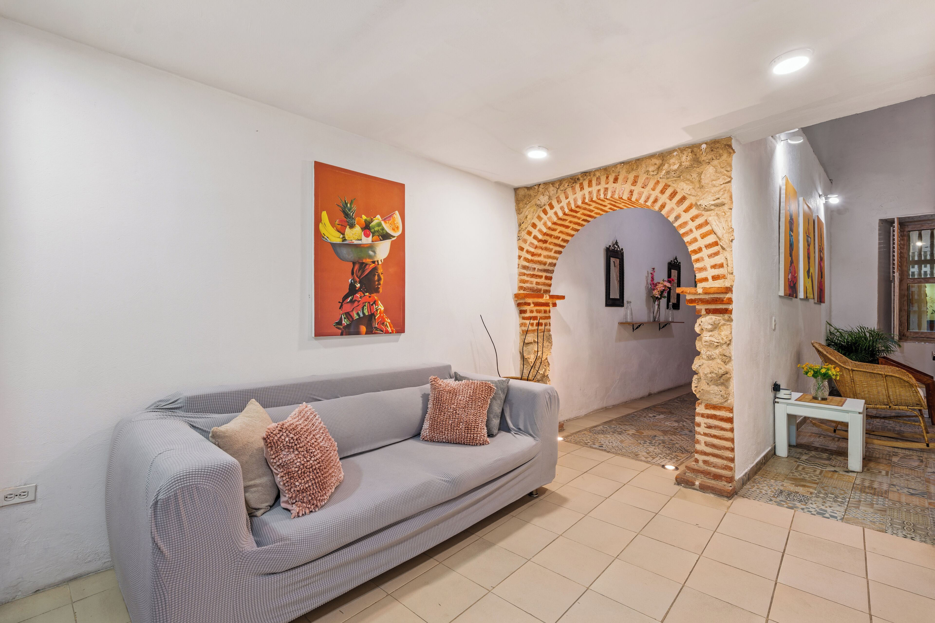 Un soggiorno con un divano grigio, un dipinto decorativo a parete, un arco in mattoni e un tavolino con un vaso.