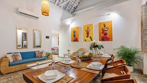Un comedor con una mesa de madera dispuesta para una comida, rodeado de mobiliario de mimbre y plantas en macetas.