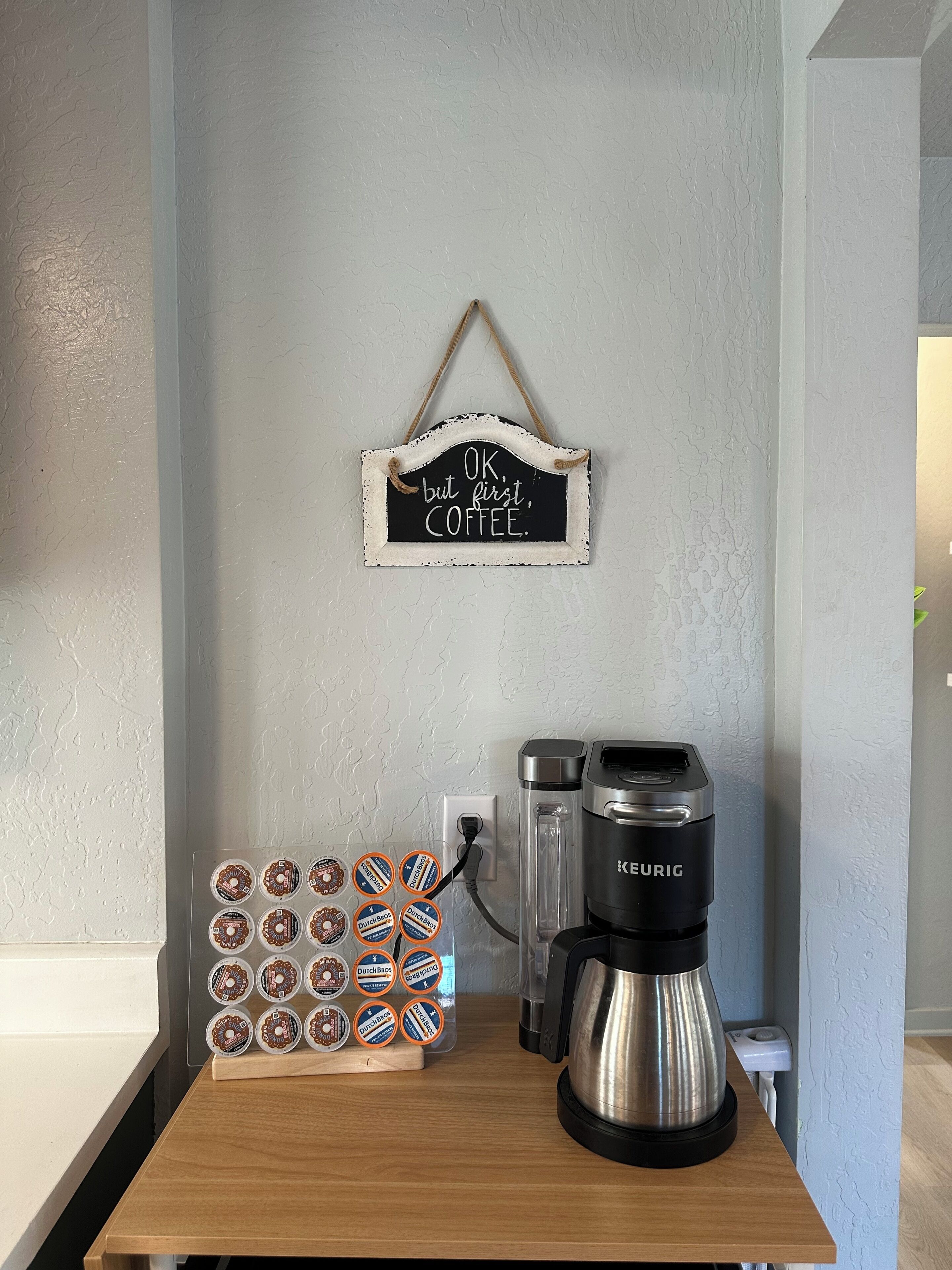 Un coin café avec une pancarte indiquant « D’accord, mais d’abord, du CAFÉ », une machine à café Keurig et des dosettes de café de la marque Dutch Bros.
