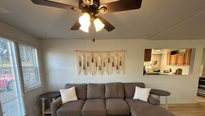 A modern living room with a sectional sofa, a ceiling fan, and a macrame wall hanging.