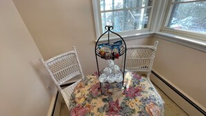 Ein Esstisch mit Blumenmuster-Tischdecke, umgeben von weißen Stuhlgestellen, und eine dekorative Leuchte in der Mitte.