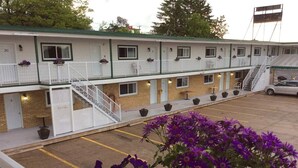 Un motel composé d’un bâtiment à deux étages, d’un parking et d’une rangée de plantes en pot.