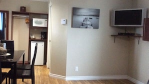 Un espace de vie compact comprenant un coin repas, une kitchenette et un téléviseur fixé au mur.