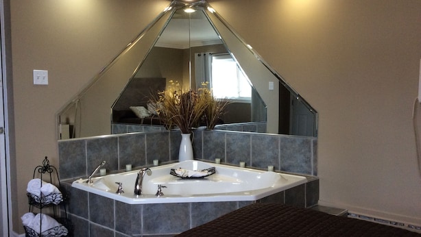 Une salle de bain moderne avec une baignoire sur pieds, un grand miroir et un vase contenant des plantes séchées.