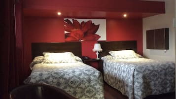A hotel room with two beds, a nightstand, a lamp, and a large floral artwork on the wall.