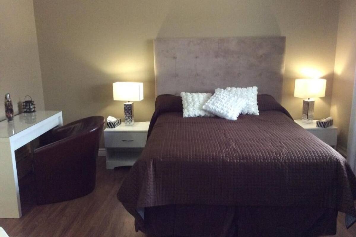 A hotel room with a large bed, two bedside tables with lamps, a small desk, and a chair.