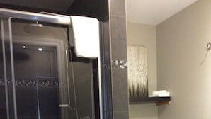 Une salle de bain avec une douche à parois de verre, des toilettes et une étagère contenant des articles de toilette.