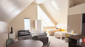 A modern, well-lit room with a loft bed, a dining area with a round table and chairs, and a kitchenette with a countertop. - Cozy Coach House - Step Outside to Frank Lloyd Wright Architectural Icons! (Oak Park)