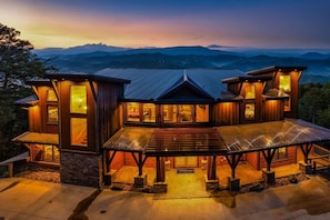 Ein großes, mehrstöckiges Holzhaus mit einer markanten Veranda und großen Fenstern, umgeben von Bergen.