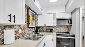 Una cocina moderna con armarios blancos, electrodomésticos de acero inoxidable y azulejos decorativos en la pared.