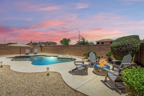 A backyard with a swimming pool, lounge chairs, a fire pit, and a brick wall. - Large Single Story in Surprise with Pool Heat Included, Mins. from Loop 303 (Surprise)
