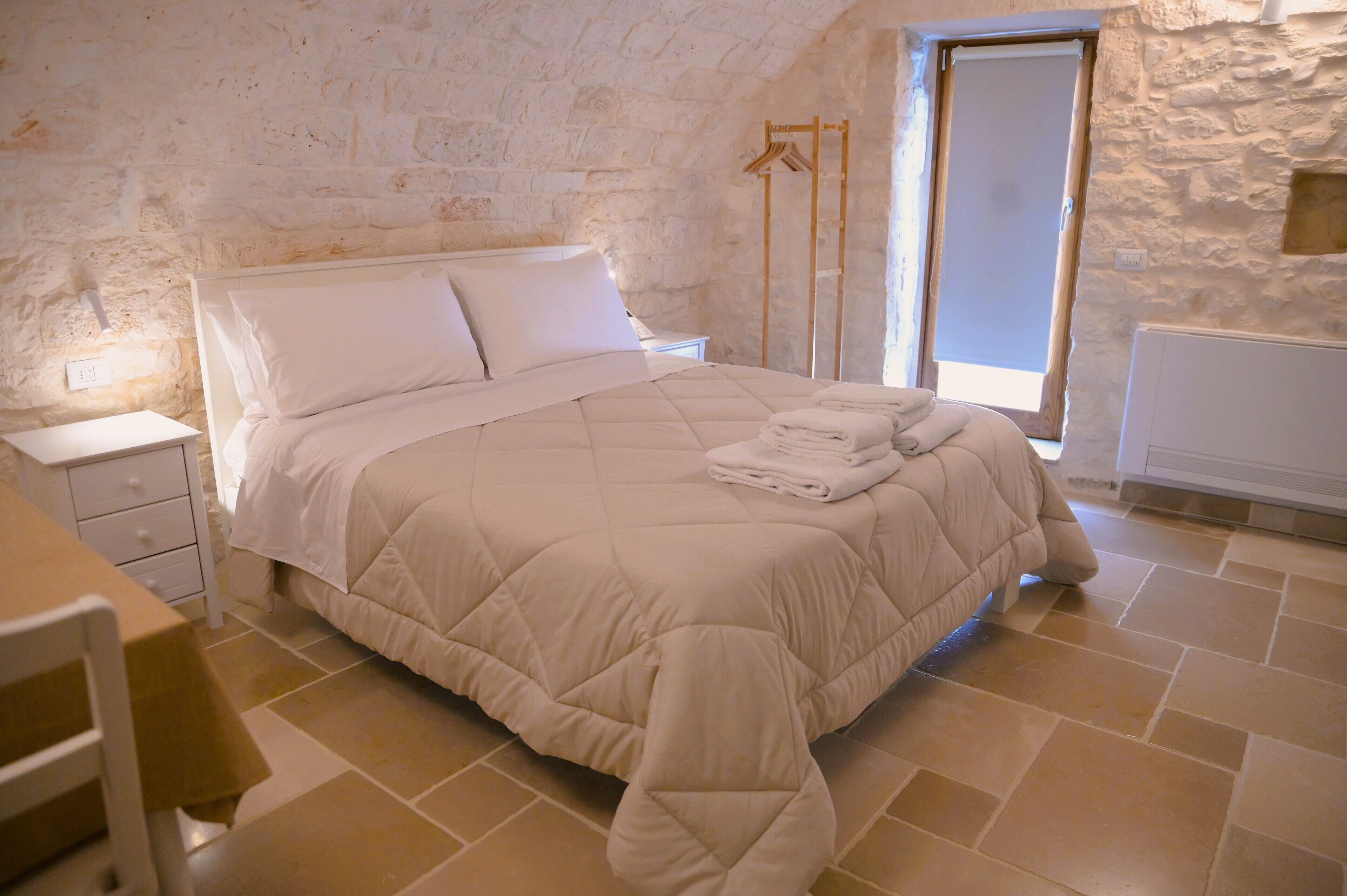 Una camera da letto con un letto, un comodino, una sedia e una finestra.