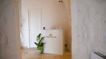 Una reception con la segnaletica Campanile Inn, una pianta in vaso e una porta in un corridoio con pareti in pietra e pavimento piastrellato.