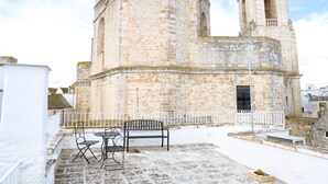 Un bâtiment en pierre doté d’une tour, d’une balustrade blanche et d’un espace extérieur aménagé pour s’asseoir.
