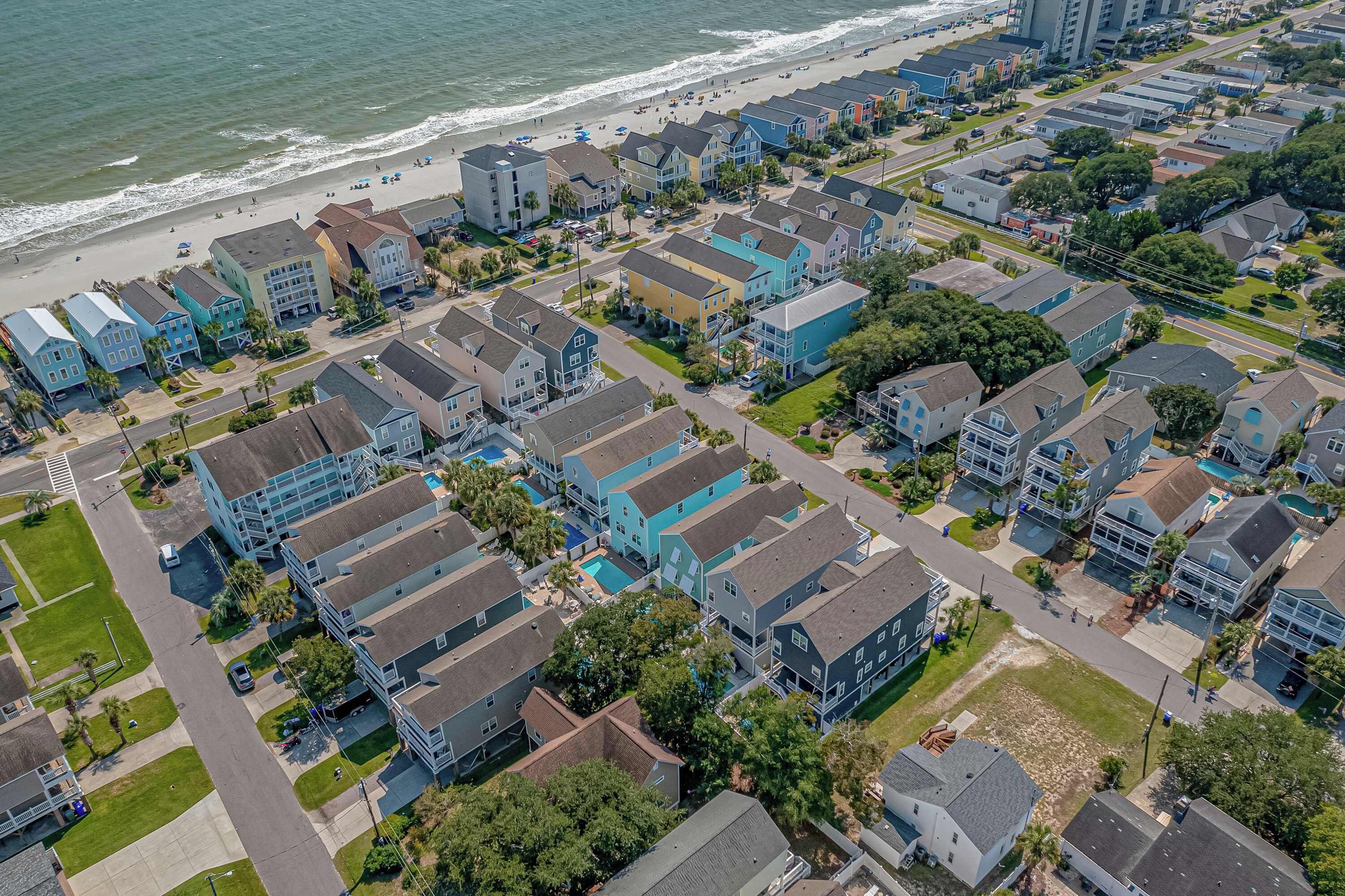 An aerial view of a coastal residential area with multi-story buildings, a beach, and a clear road network.