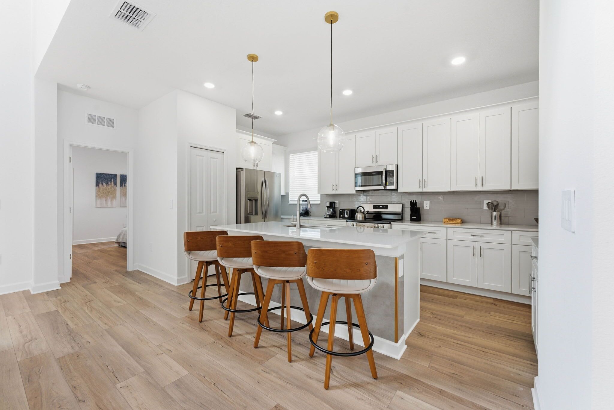 A modern kitchen with white cabinets, a central island with bar stools, stainless steel appliances, and pendant lighting.