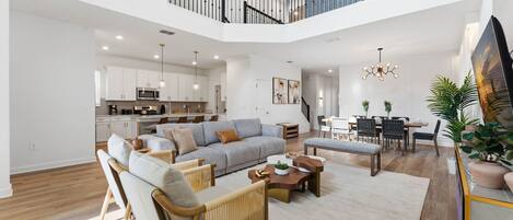 A spacious living area with a large gray sectional sofa, wooden chairs, and a coffee table. A dining area with a table and chairs is visible in the background.
