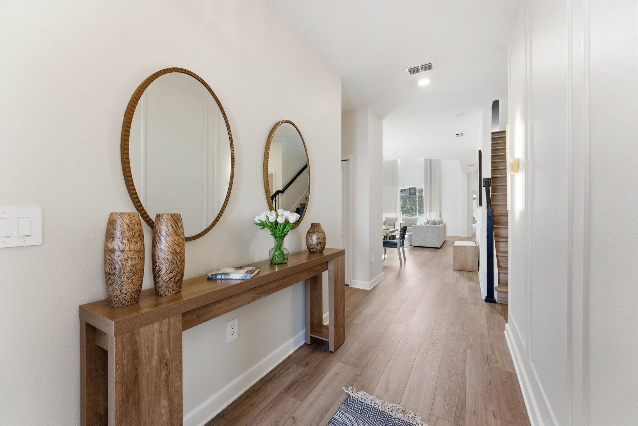 A hallway with a wooden console table, two mirrors, and decorative vases.